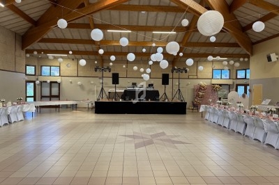 Salle de réception décorée avec des lanternes suspendues, tables dressées et une scène équipée pour un événement.