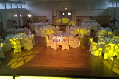 Salle de réception décorée avec des tables rondes dressées et un éclairage jaune créant des motifs au sol.