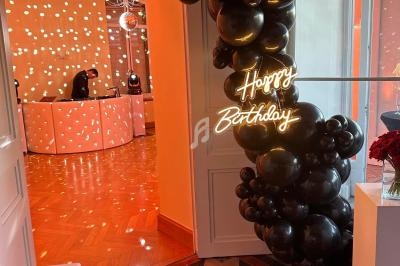 Décoration d'anniversaire avec ballons noirs et enseigne lumineuse ’Happy Birthday’ dans une pièce éclairée de lumières…