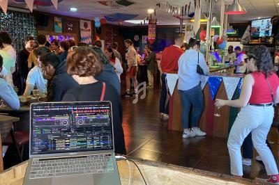 Des personnes discutent et boivent dans un bar décoré, avec un ordinateur affichant un logiciel de mixage au premier plan.