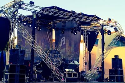 Scène extérieure avec structure métallique, éclairages et équipements audio installés pour un événement.