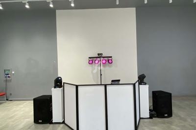 Poste de DJ avec une table blanche, des enceintes noires, des projecteurs colorés et un éclairage d'ambiance dans une salle…