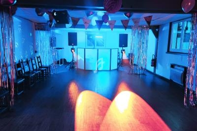 Salle de fête décorée avec guirlandes et lumières colorées, équipée d’une piste de danse et d’un espace DJ.