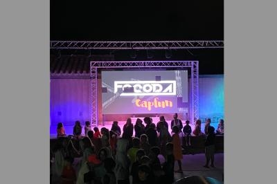 Un groupe de personnes debout devant un écran géant illuminé affichant des visuels colorés, en extérieur la nuit.