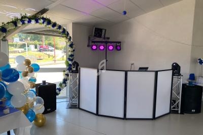 Décoration de salle avec arche de ballons, éclairage coloré et espace DJ équipé de haut-parleurs et panneaux lumineux.