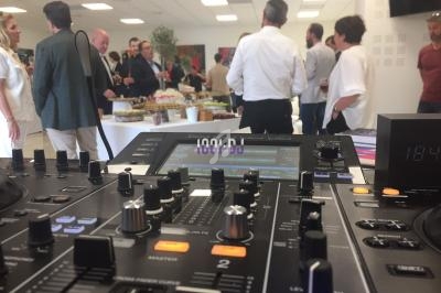 Vue d'une table de mixage en premier plan lors d'un événement avec des invités discutant autour d'un buffet.