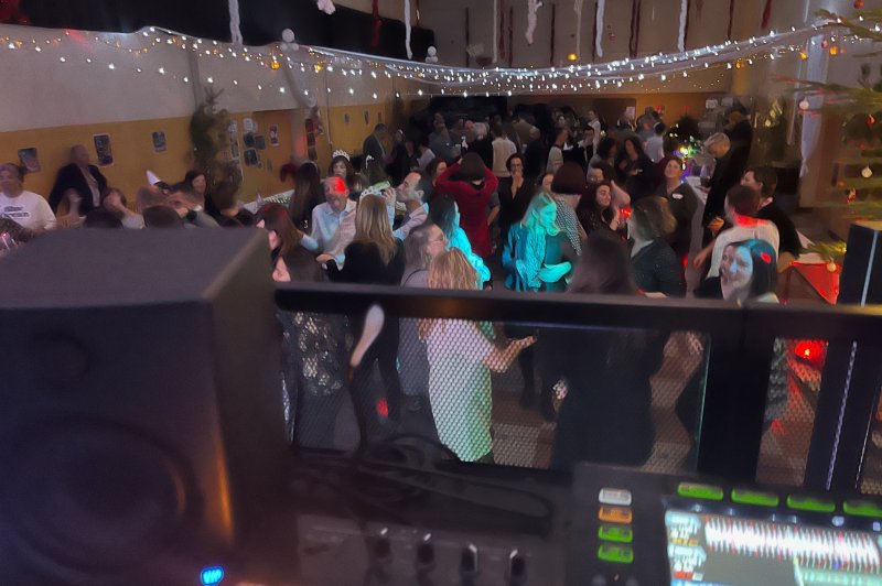 Salle animée avec des personnes dansant sous des guirlandes lumineuses, vue depuis une table de mixage.