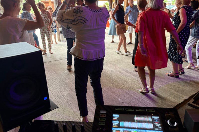 Personnes dansant dans une salle ouverte, vue depuis une table de mixage avec un écran allumé au premier plan.