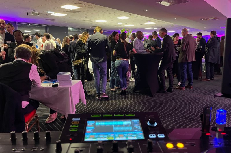 Groupe de personnes discutant lors d'un événement en intérieur, avec une table de mixage visible au premier plan.