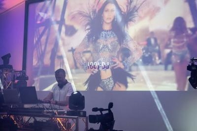 Un DJ mixe sur scène devant un écran géant diffusant une vidéo d'une danseuse en costume scintillant.