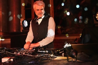 Un homme en costume joue de la musique sur une table de mixage dans une salle éclairée par des lumières colorées.