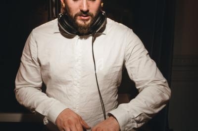 Homme portant un casque audio autour du cou, vêtu d'une chemise blanche, ajustant un équipement devant lui.