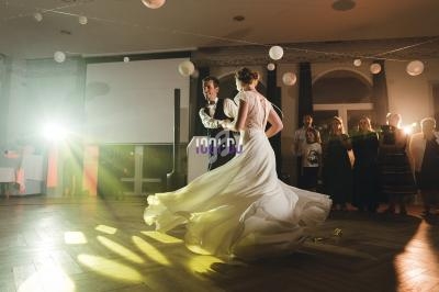 Un couple danse dans une salle éclairée, entouré d'invités observant en arrière-plan.