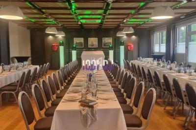 Salle de réception aménagée avec de longues tables dressées pour un repas, éclairage vert au plafond.