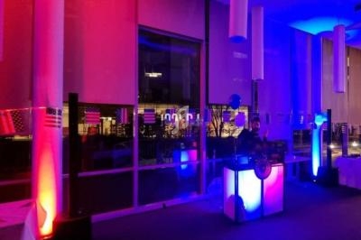 Installation lumineuse avec des éclairages colorés rose et bleu, entourant une table de mixage dans une salle vitrée.