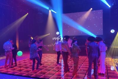 Personnes dansant sur une piste lumineuse avec des jeux de lumière colorés et un écran en arrière-plan.