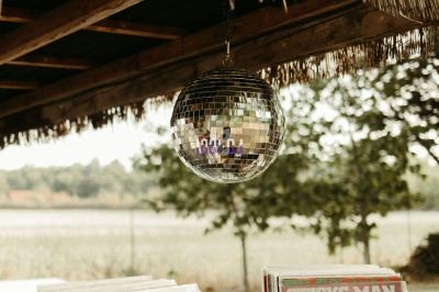 Boule à facettes suspendue sous un toit en chaume, avec des caisses de vinyles en bois au premier plan.