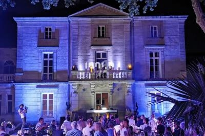 Façade d'un bâtiment éclairé en bleu la nuit, avec une foule rassemblée devant sous des arbres.