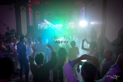 Groupe de personnes dansant dans une salle sombre avec des lumières colorées et un DJ en arrière-plan.
