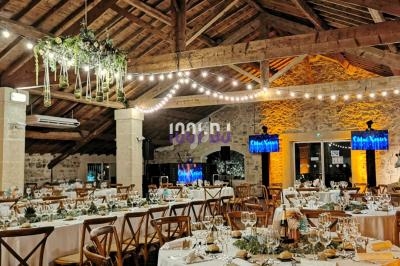 Salle de réception décorée avec des tables dressées, des guirlandes lumineuses suspendues et un plafond en bois apparent.