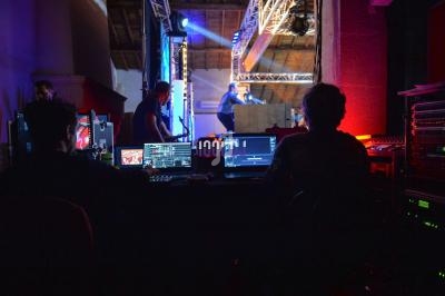 Techniciens supervisant des équipements audiovisuels lors d'un événement sur une scène éclairée.