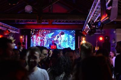 Salle de fête avec des invités dansant devant un DJ et un écran lumineux sous un éclairage coloré.