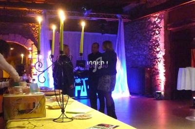 Des personnes discutent près d'une table dressée dans une salle éclairée avec des bougies et des lumières colorées.