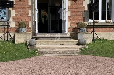 Entrée d'un bâtiment en briques avec porte ouverte, haut-parleurs et pots de fleurs sur les marches.