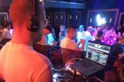 Un DJ mixe de la musique sur son ordinateur portable dans une salle de concert animée avec des lumières colorées.