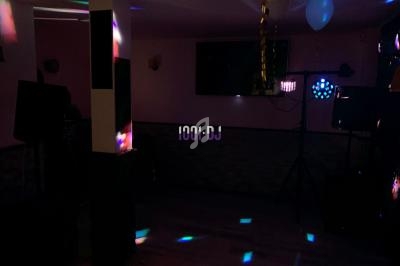 Salle sombre avec éclairage coloré de type discothèque, ballons suspendus et équipement de sonorisation visible.