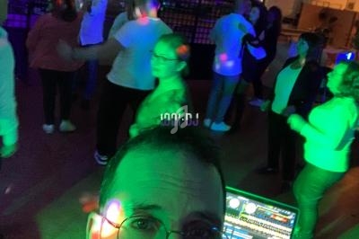 Un DJ anime une soirée dansante avec des lumières colorées, des participants dansent en arrière-plan.