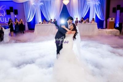 Un couple danse leur première danse de mariage sur une piste entourée de fumée, avec des invités en arrière-plan.