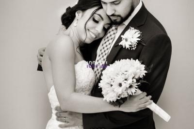 Un couple en tenue de mariage s'enlace tendrement devant un mur clair.