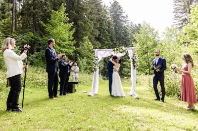 Un couple s'embrasse sous une arche décorée lors d'une cérémonie de mariage en plein air, entouré d'invités.