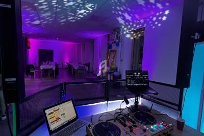 Console de DJ avec platines et ordinateur, éclairages colorés et salle décorée en arrière-plan.