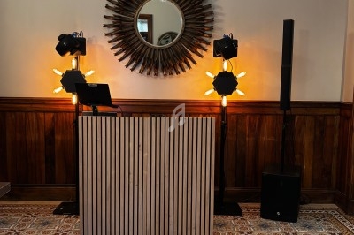 Pupitre en bois devant un mur avec miroir rond, éclairages décoratifs et équipement audio.