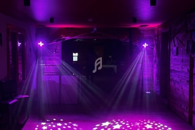 Salle sombre éclairée par des projecteurs violets diffusant des faisceaux lumineux et des motifs étoilés au sol.