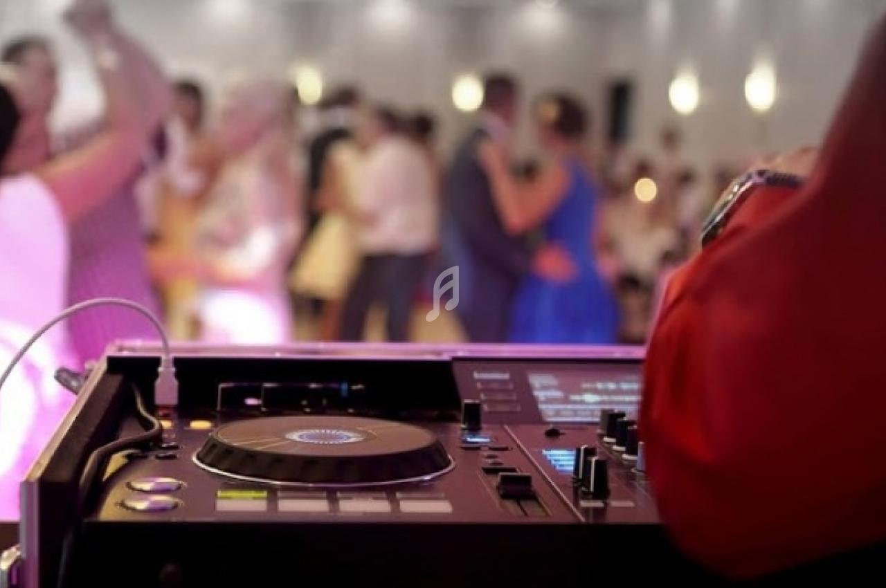 Vue rapprochée d'une table de mixage de DJ, avec des personnes dansant en arrière-plan dans une salle éclairée.