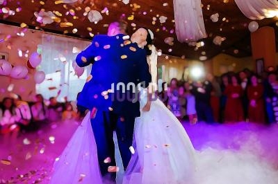 Un couple danse au centre d'une salle décorée, entouré de fumée et de confettis, devant des invités.