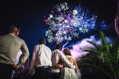 Un groupe de personnes, dont un couple en tenue de mariage, regarde un feu d'artifice éclatant dans le ciel nocturne.