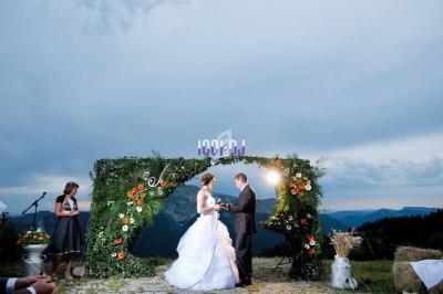 Un couple échange ses vœux sous une arche fleurie en extérieur, avec une vue sur des montagnes au crépuscule.