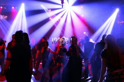 Personnes dansant dans une salle de concert sombre éclairée par des projecteurs colorés et des jeux de lumière.