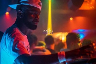 Un DJ mixe sur une table de mixage dans une ambiance de boîte de nuit avec éclairages colorés.