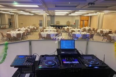 Vue d'une salle de réception avec tables dressées, prise depuis une régie DJ équipée de matériel audio et d'un ordinateur.