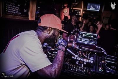 Un DJ mixant sur des platines dans un club animé avec des écrans et un public en arrière-plan.