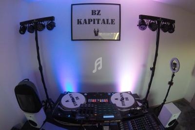 Deux platines, une table de mixage et des éclairages installés dans une pièce avec un cadre ’BZ KAPITALE’ au mur.