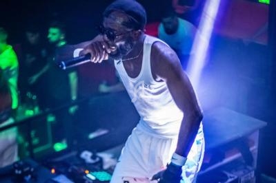 Un chanteur sur scène, vêtu de blanc, tenant un micro, éclairé par des lumières vives dans une ambiance de concert.