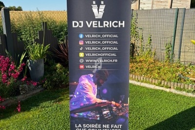 Roll-up publicitaire avec le logo ’DJ Velrich’, des réseaux sociaux et une photo de DJ en soirée, placé dans un jardin.