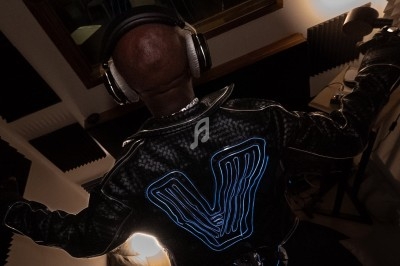 Un homme de dos portant un casque audio et une veste lumineuse dans un studio d'enregistrement.