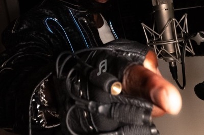 Un homme portant des lunettes de soleil et un casque audio pointe vers l'objectif dans un studio d'enregistrement.